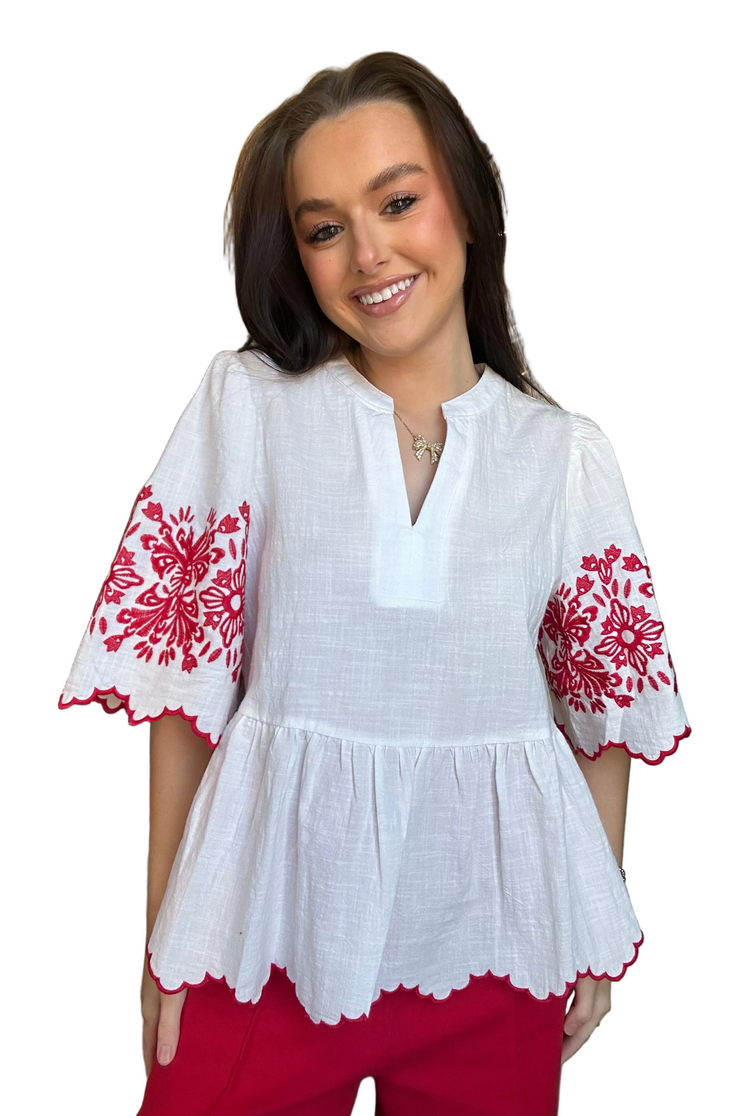Woman wearing a white blouse with red floral embroidery on a white background