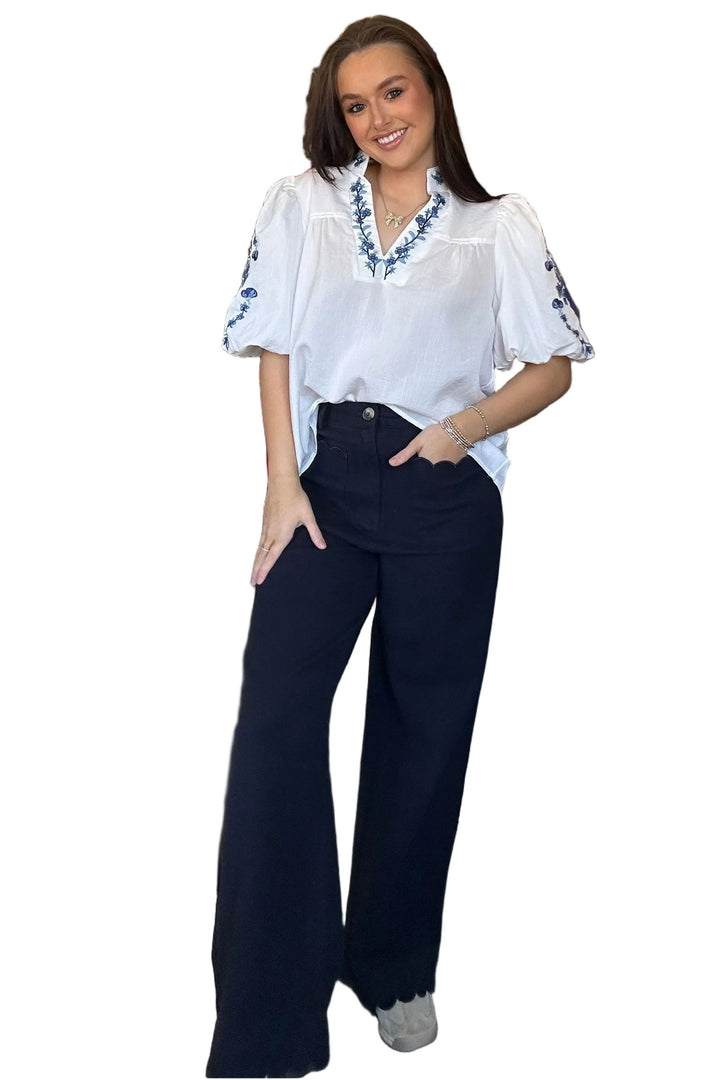 Woman wearing a white blouse with blue embroidery and dark blue pants on a white background