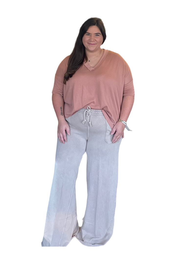 Woman wearing a clay top and light tan pants on a white background