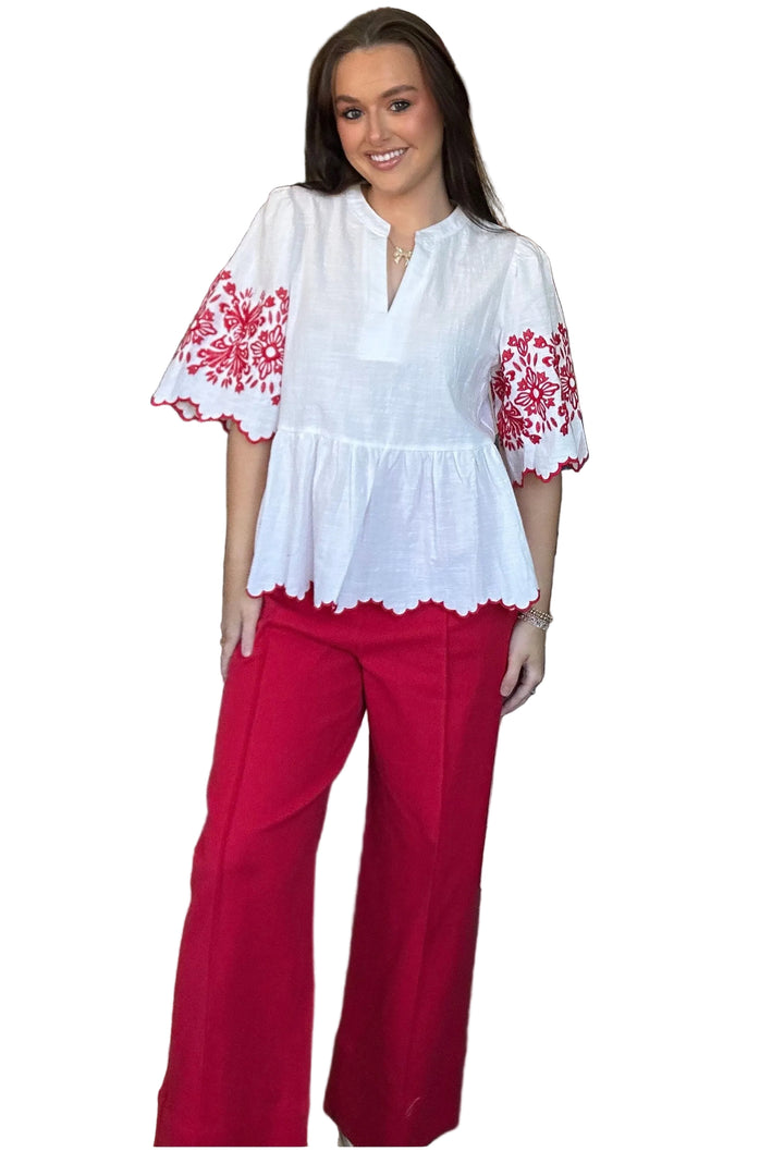 Woman wearing a white blouse with red floral embroidery and red pants on a white background