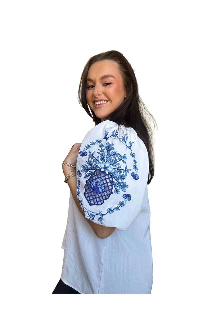 Woman wearing a white blouse with blue floral embroidery on a white background