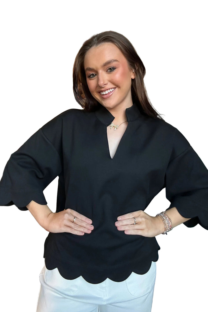 Woman wearing a black top with scalloped edges in a clothing store.