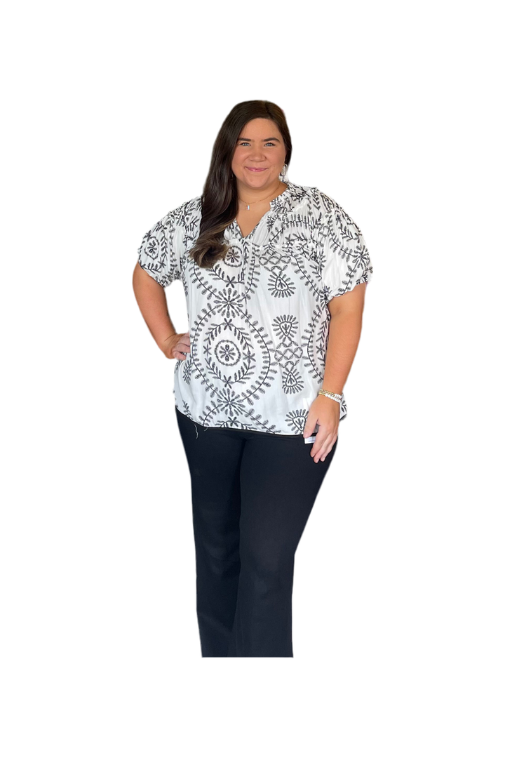 Woman wearing a patterned blouse and dark pants on a white background