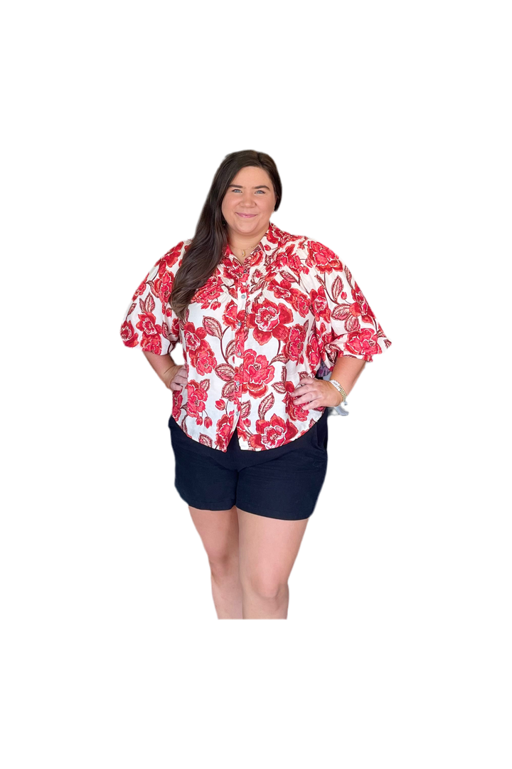 Woman wearing a red and white floral shirt with navy shorts on a white background
