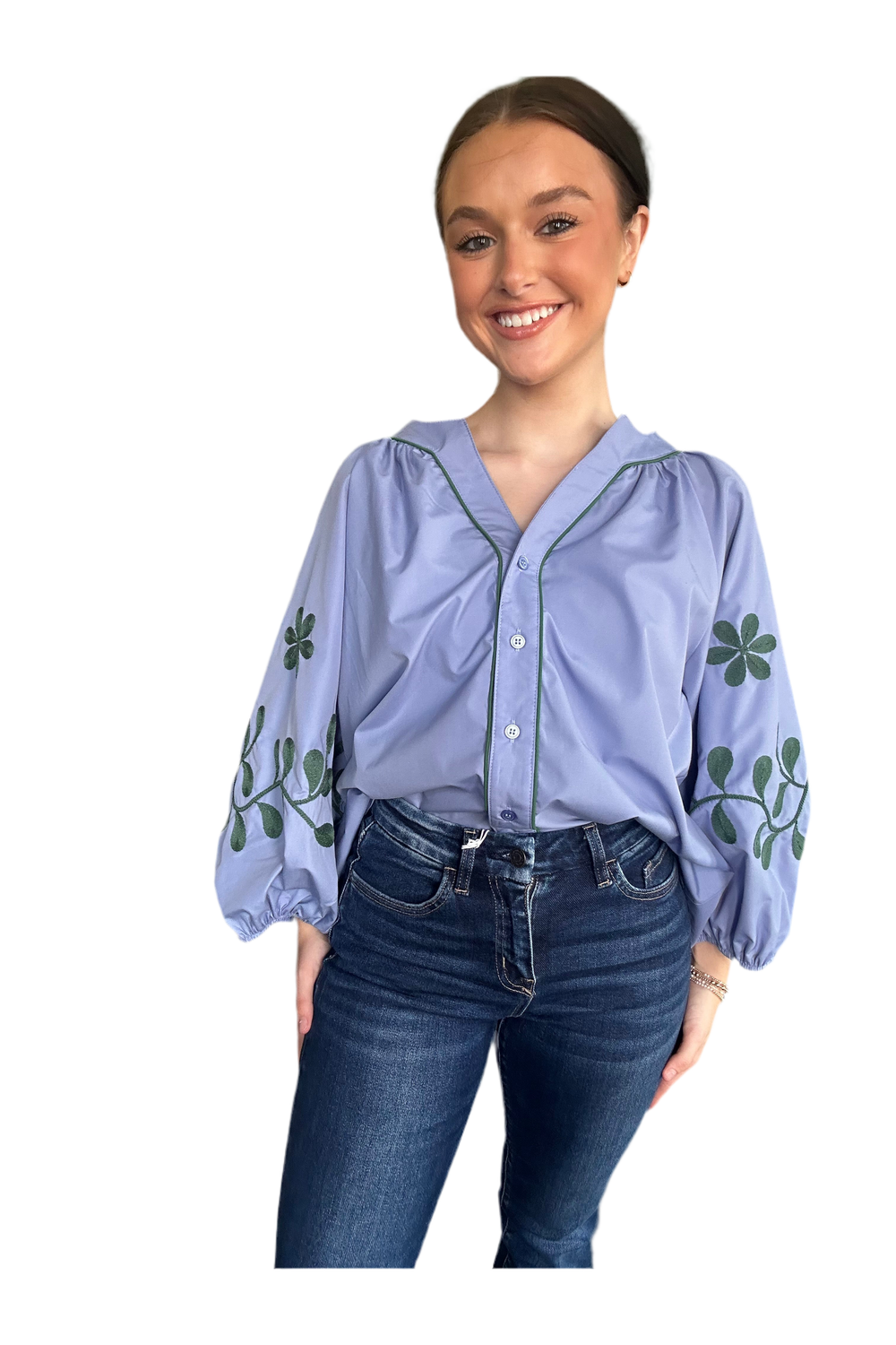 Woman wearing a light blue blouse with floral embroidery and dark jeans on a white background