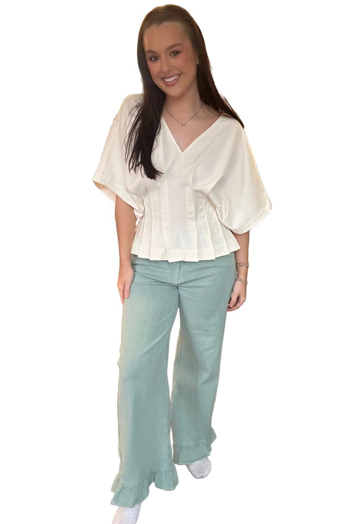 Woman in a white blouse and light green pants standing in a store.