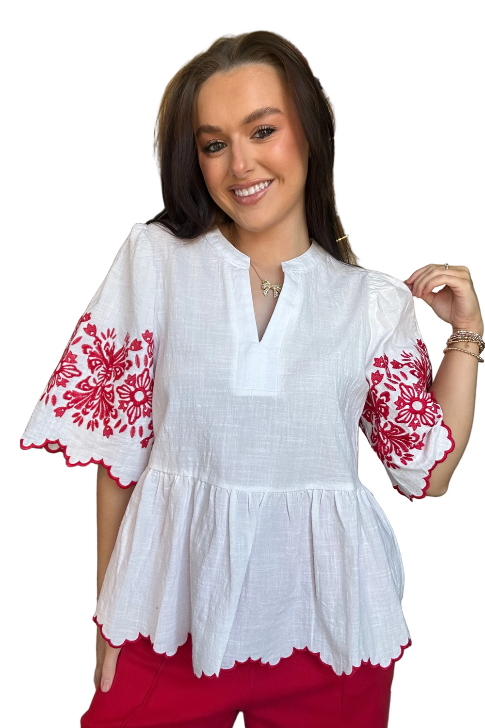 Woman wearing a white blouse with red embroidery and red pants on a white background