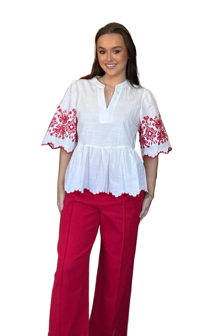Woman in a white blouse with red floral patterns and red pants standing in a store.