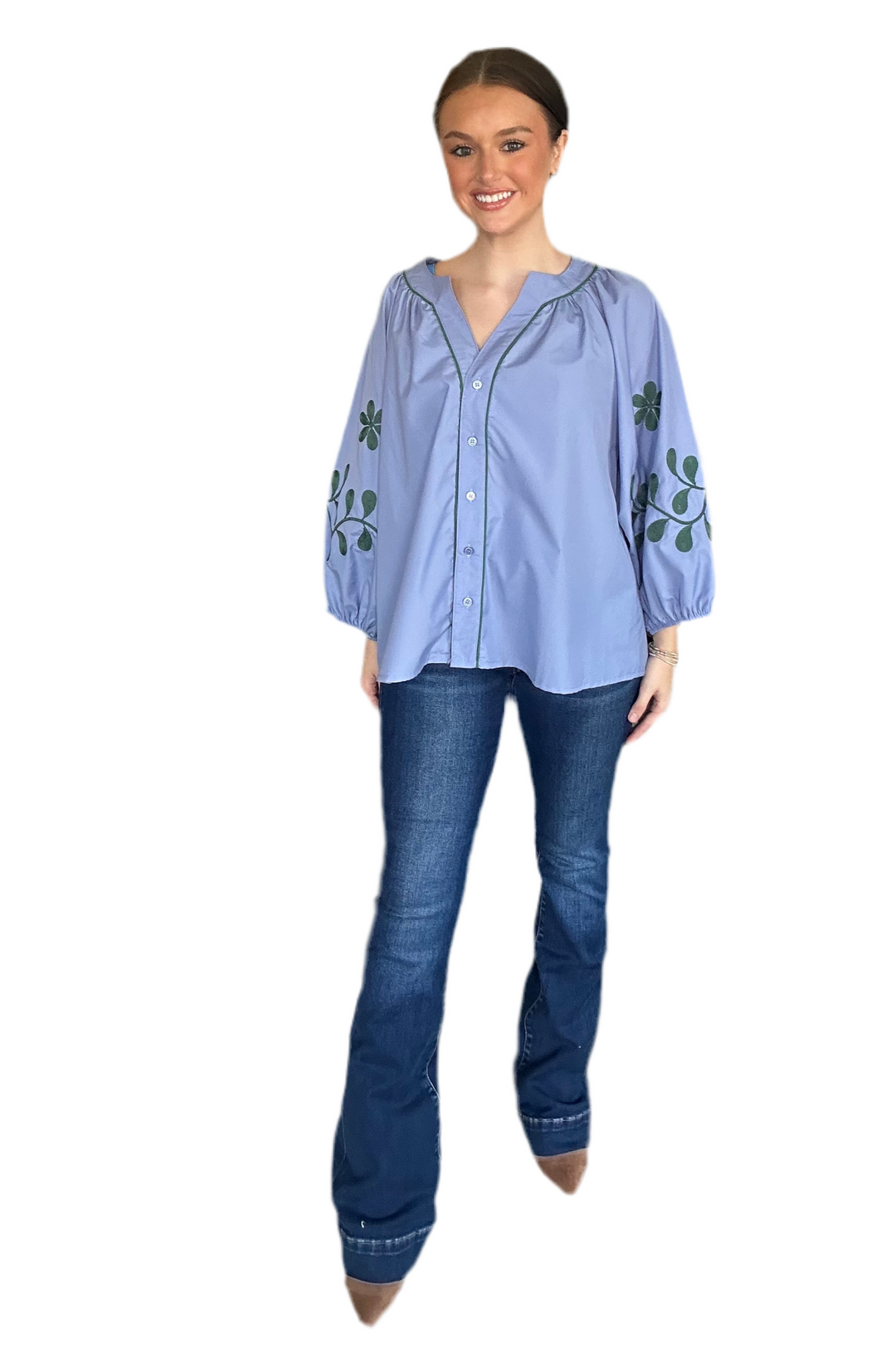 Woman wearing a light blue blouse with floral embroidery and dark blue jeans on a white background
