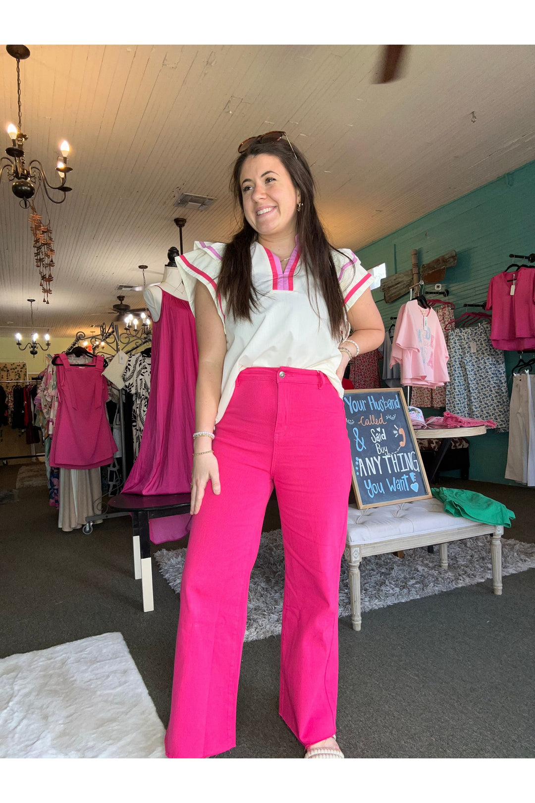 Woman in a store wearing pink pants and a white top, surrounded by clothing racks.