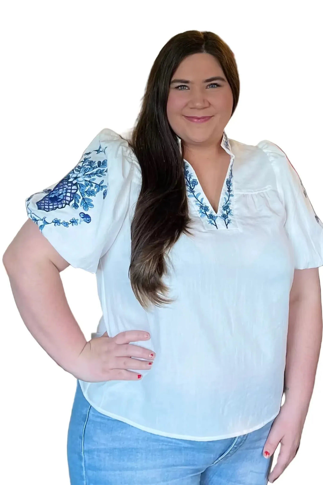 Woman wearing a white blouse with blue embroidery and blue jeans on a white background