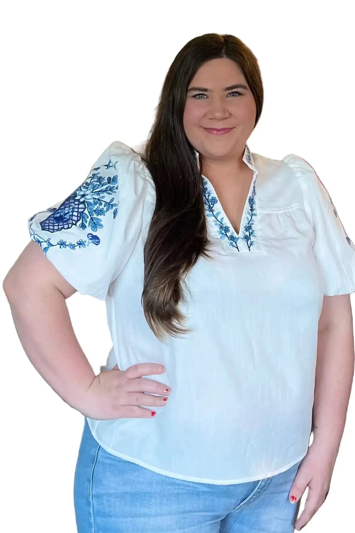 Woman wearing a white blouse with blue embroidery and blue jeans on a white background