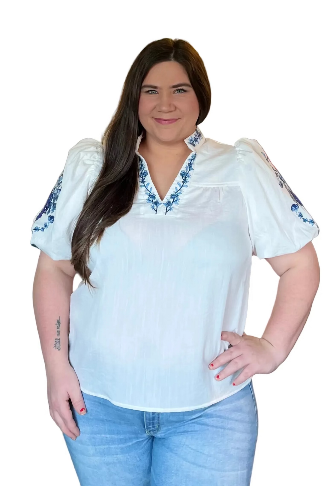Woman wearing a white blouse with blue embroidery and blue jeans on a white background