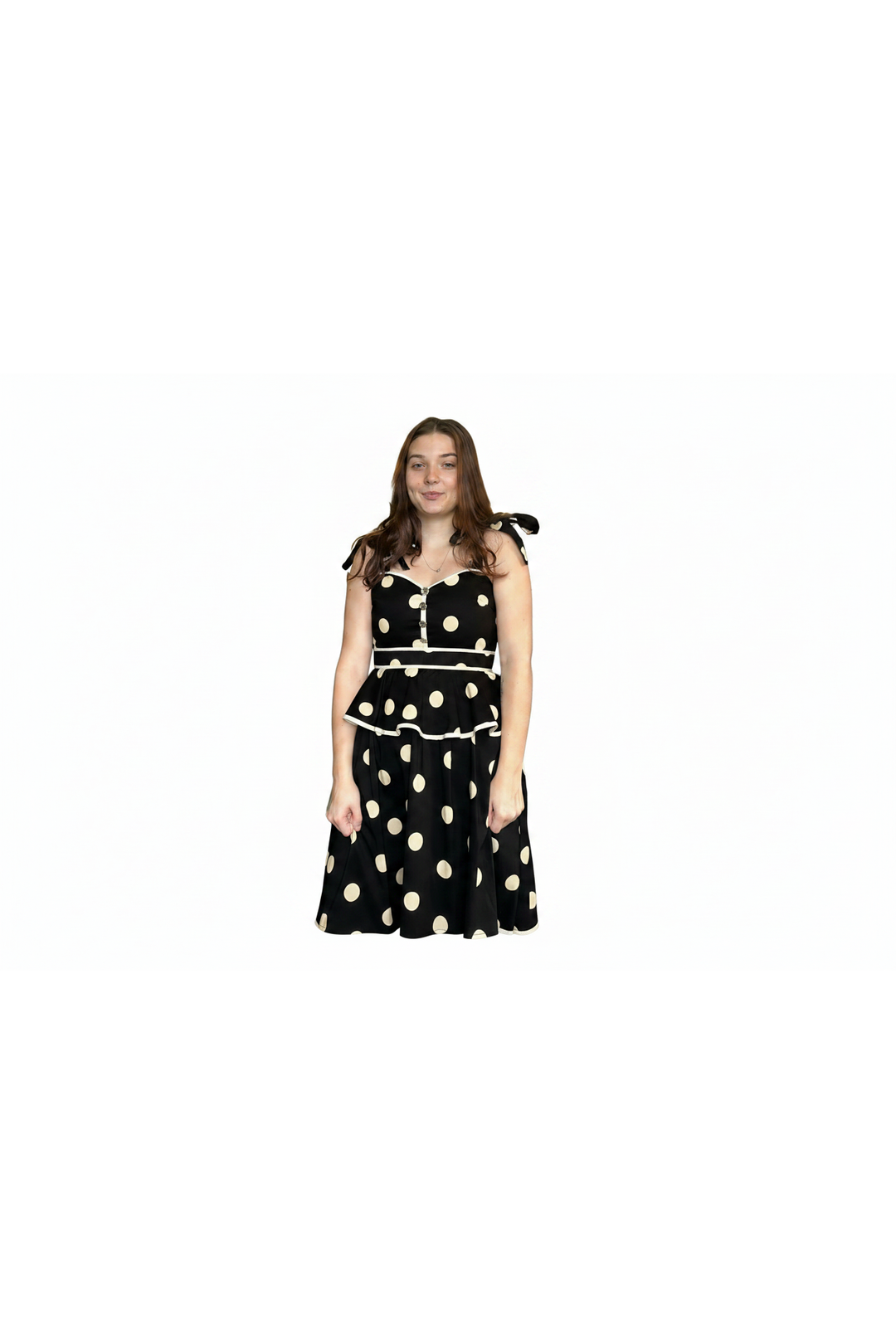 A woman modeling a black sleeveless dress with large beige polka dots, a sweetheart neckline, and tie details on the shoulders, set against a plain white background.